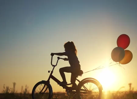 Child riding a bike with balloons attached at twilight